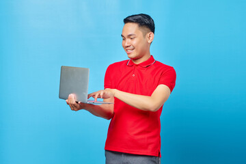 Portrait of smiling young handsome man holding and using a laptop on blue background