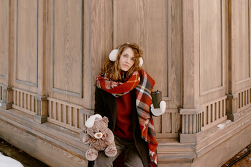 Christmas. Young woman in winter clothes and fur earmuffs. Girl with teddy bear and mulled wine