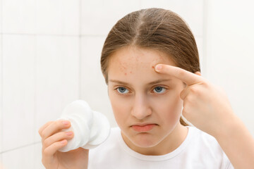 face of a teenage girl with pimples, she looks at herself in the mirror and takes care of her skin,...