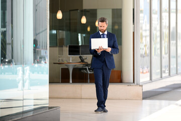 Business man holding laptop standing on the street near business office building.