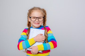 a cute little girl in a multicolored sweater and glasses holds a book on a white background ,...