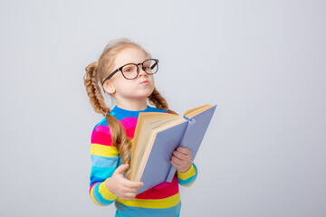 a cute little girl in a multicolored sweater and glasses holds a book on a white background ,...
