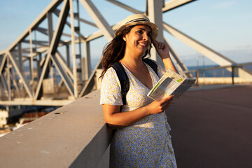 Happy young woman with a city map travelling. Young beautiful female traveler, standing on the street and looking at the map..