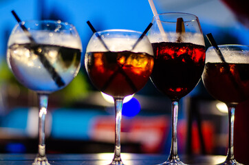 Beautiful row line of different colored alcohol cocktails on a party, martini, vodka,and others on decorated catering bouquet table on open air event, picture with beautiful bokeh