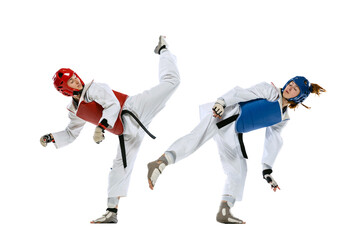 Dynamic portrait of two young women, taekwondo athletes training together isolated over white...