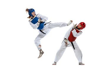 Naklejka na ściany i meble Dynamic portrait of two young women, taekwondo practitioners training together isolated over white background. Concept of sport, skills
