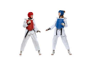 Studio shot of of two young women, taekwondo athletes practicing together isolated over white...