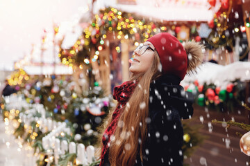 Winter portrait young beautiful happy woman in wearing stylish warm clothes, snow and bokeh lights. Concept travel Christmas holidays Europe city