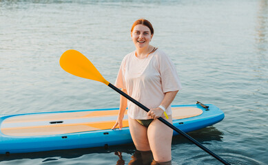 Happy woman studing on paddle board at sunset. Outdoor water sports. Rent of equipment for swimming in the ocean or sea