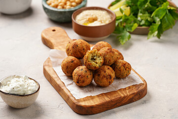 Traditional oriental chickpea deep fried falafel on a wooden board, tzatziki yoghurt sauce, hummus, fresh lime and green cilantro on light surface