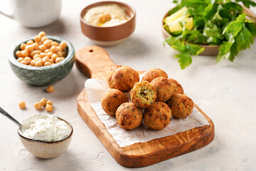 Traditional oriental chickpea deep fried falafel on a wooden board, tzatziki yoghurt sauce, hummus, fresh lime and green cilantro on light surface