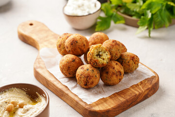 Traditional oriental chickpea deep fried falafel on a wooden board, tzatziki yoghurt sauce, hummus and fresh green cilantro on light surface