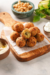 Traditional oriental chickpea deep fried falafel on a wooden board, tzatziki yoghurt sauce, hummus, fresh lime and green cilantro on light surface