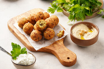 Traditional oriental chickpea deep fried falafel on a wooden board, tzatziki yoghurt sauce, hummus, fresh lime and green cilantro on light surface
