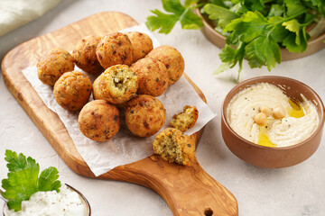 Traditional oriental chickpea deep fried falafel on a wooden board, tzatziki yoghurt sauce, hummus, fresh lime and green cilantro on light surface