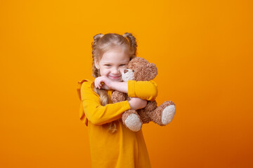 cute little girl holding a teddy bear on a yellow background, hugging