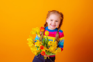a cute little girl in a multicolored sweater holds a bouquet of spring flowers on a yellow background