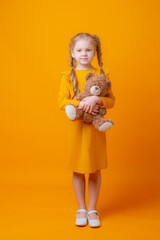 cute little girl holding a teddy bear on a yellow background, hugging