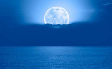 Night sky with full bright moon in the clouds, blue sea in the foreground "Elements of this image furnished by NASA"