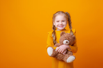 cute little girl holding a teddy bear on a yellow background, hugging
