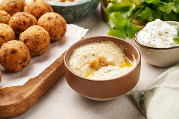 Traditional oriental chickpea deep fried falafel on a wooden board, tzatziki yoghurt sauce, hummus, fresh lime and green cilantro on light surface
