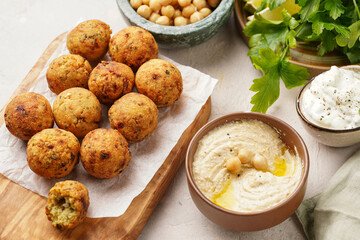Traditional oriental chickpea deep fried falafel on a wooden board, tzatziki yoghurt sauce, hummus, fresh lime and green cilantro on light surface