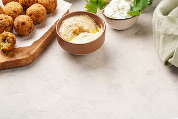 Traditional oriental chickpea deep fried falafel on a wooden board, tzatziki yoghurt sauce, hummus, fresh lime and green cilantro on light surface, negative space fo text
