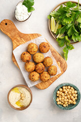 Traditional oriental chickpea deep fried falafel on a wooden board, tzatziki yoghurt sauce, hummus, fresh lime and green cilantro on light surface, top view