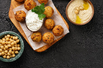 Traditional oriental chickpea deep fried falafel on a wooden board, tzatziki yoghurt sauce, hummus, fresh lime and green cilantro on black surface, copy space