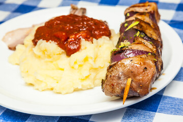 Meat kebab with onions on a wooden stick, on a white plate with mashed potatoes.