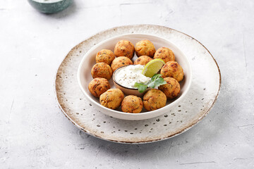 Traditional oriental chickpea deep fried falafel in a deep bowl with tzatziki yoghurt sauce, hummus, fresh lime and green cilantro on light grey concrete surface