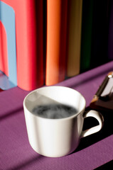 White ceramic mug with hot coffee on purple work desk and books with lgbt movement colors