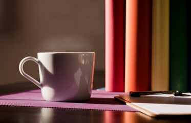 White ceramic mug with hot coffee on purple work desk and books with lgbt movement colors