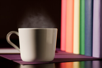 White ceramic mug with hot coffee on purple work desk and books with lgbt movement colors