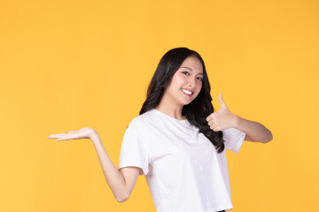 Beautiful Asian woman wearing casual clothes smile and pointing finger to an empty palm isolated on yellow background studio portrait.