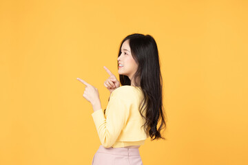 Beautiful Asian woman wearing yellow t-shirt smile and pointing finger at copy space isolated on yellow background studio portrait.