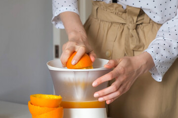 Woman is squeezing oranges using electric juicer in the kitchen making juice, closeup view. Healthy...