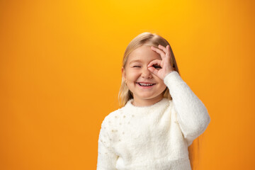 Portrait of positive kid girl show okay sign over yellow background