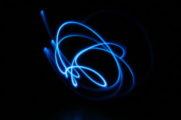 Garabatos de luz de neòn color azul, en velocidad y desenfoque, con formas diferentes forman un...