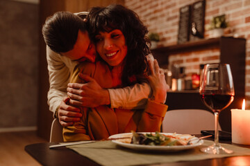 White couple hugging while having romantic dinner at home
