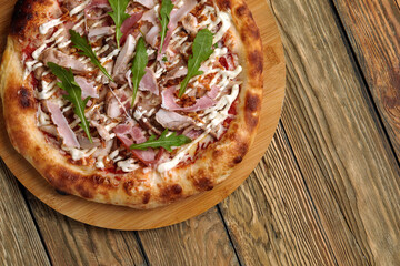 croped shot of neapolitan Pizza with Mozzarella cheese, bacon, ham, tomato sauce, chicken, Spices and Fresh arugula. Italian pizza on wooden table background