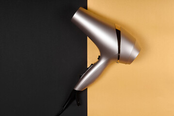 Golden hair dryer on black and yellow paper background, copy space. Top view, flat lay