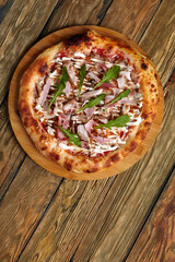 neapolitan Pizza with Mozzarella cheese, bacon, ham, tomato sauce, chicken, Spices and Fresh arugula. Italian pizza on wooden table background