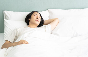 Obraz na płótnie Canvas Portrait of young Asian man lying relaxing sleeping in cozy white bed and keeping eyes closed while covered with blanket in the morning. Guy enjoy sweet dreams, peaceful time and energy power restore.