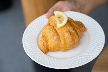 Yuzu croissant on a white ceramic plate holding a woman's hand