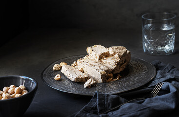 Halwa with hazelnuts and glass of water on dark grey background with napkin