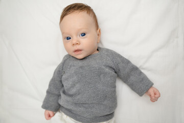 Portrait of lovely baby with blue eyes lying in bed. Baby smiling and looking up to camera. Good morning. Beautiful baby boy four months old lying on a blue soft blanket.