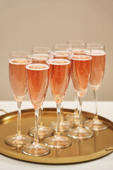 graceful glasses with pink sparkling wine on a gold tray are in a row