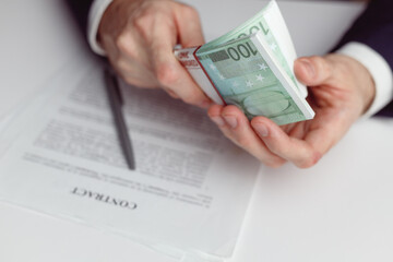 Man in suit counts wad of money before signing contract. Close up of hands with money
