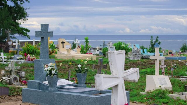 Crosses gravestones stand on the rocky shore as waves crash over the rocks. Oceanfront cemetery
